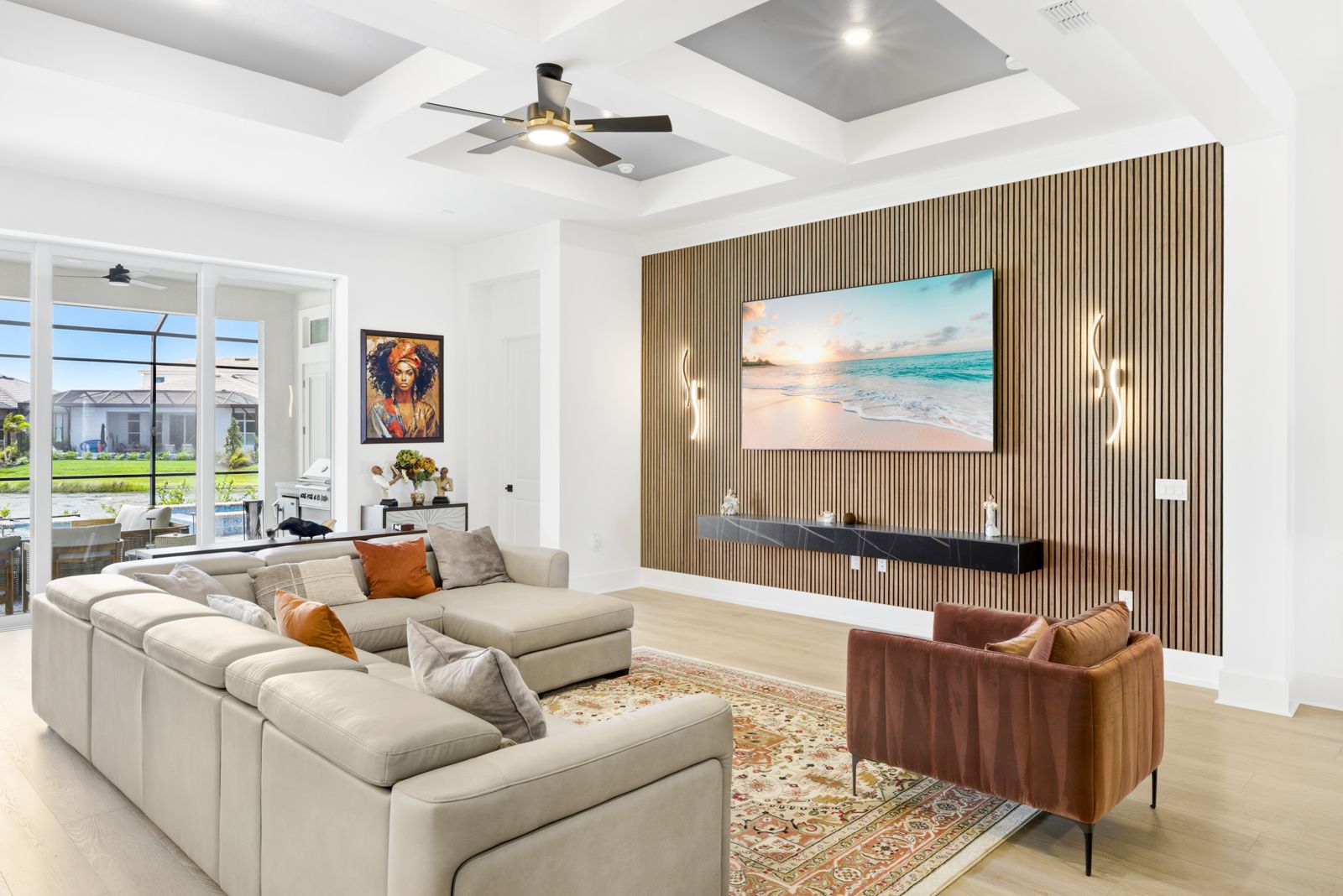 Wood slat media wall panel holding a TV with a wall sconce on each side and a floating console below, in an open great room in a Talon Preserve home