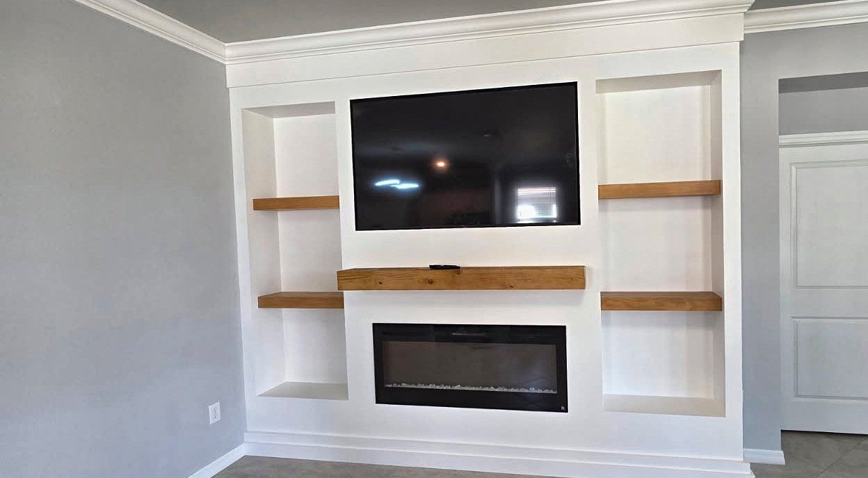 White built-in media wall with recessed side niches, floating wood shelves, a wood mantel and a linear fireplace below the TV, in a Venice, FL home